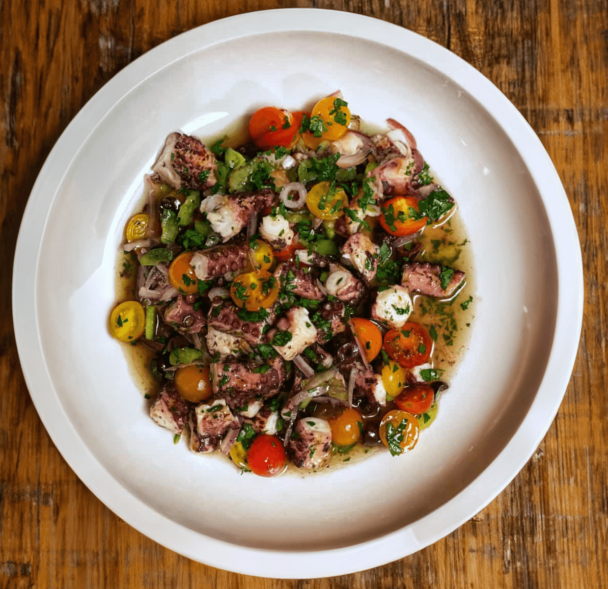 Fresh octopus salad with cherry tomatoes, herbs, and olive oil on a white plate