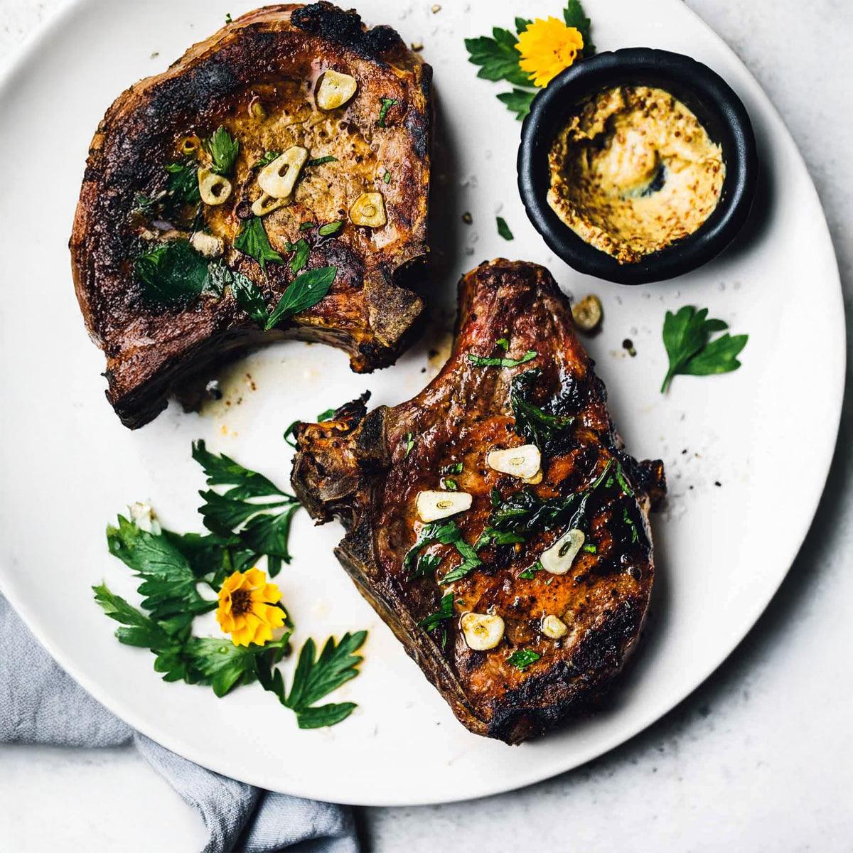 Grilled pork chops with garlic and herbs, served with dipping sauce on a white plate