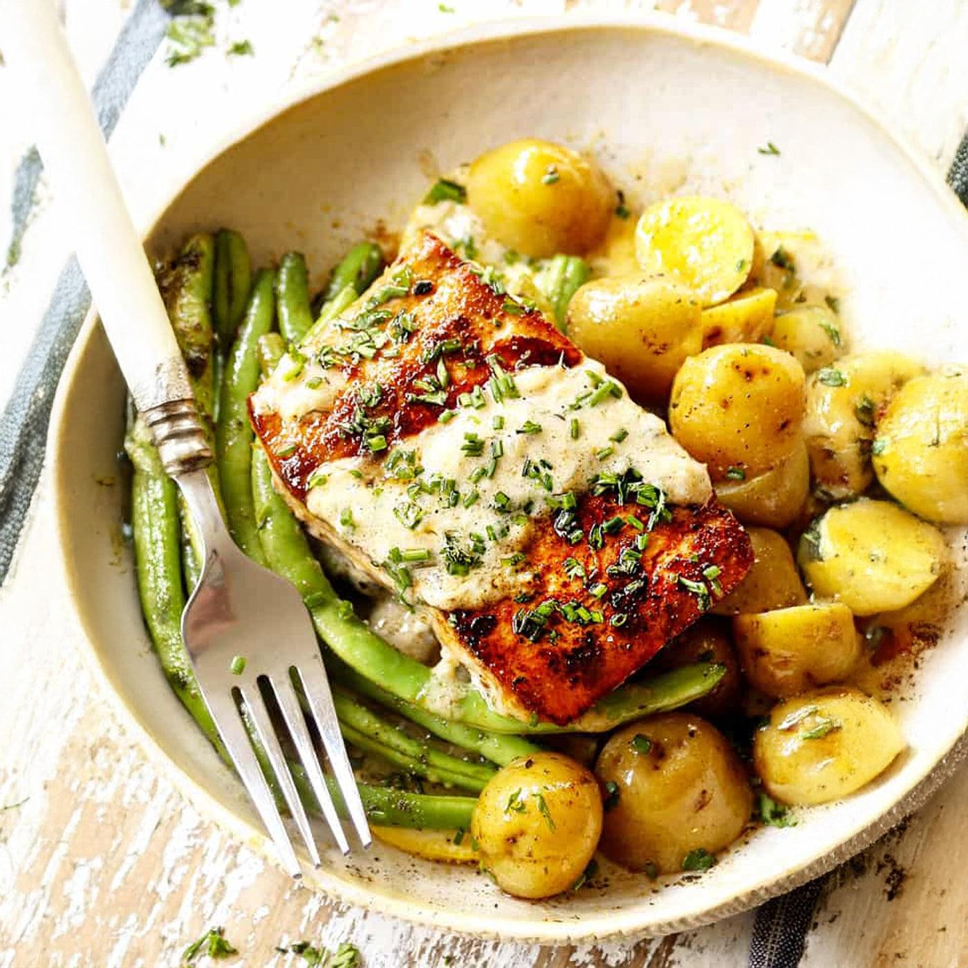 Seared salmon with creamy sauce, green beans, and baby potatoes in a rustic bowl