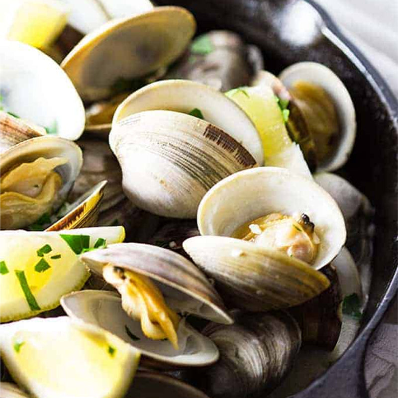 Fresh steamed clams with lemon and herbs in a cast iron skillet