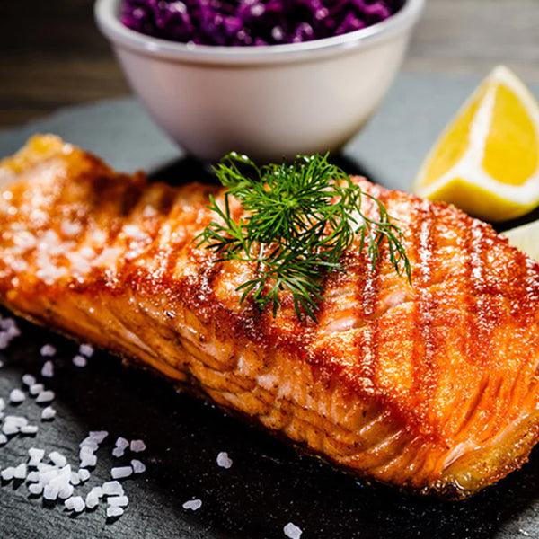 Grilled salmon fillet with dill, lemon wedge, and purple cabbage slaw, seasoned with sea salt