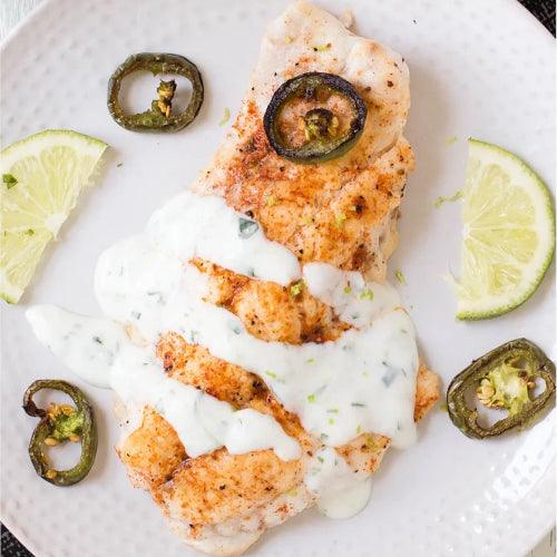 Grilled fish fillet with creamy sauce, lime wedges, and jalapeño slices — fresh seafood meal