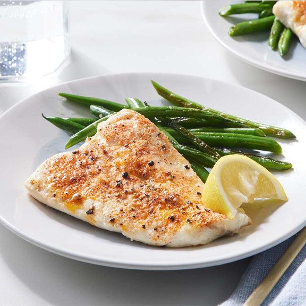 Grilled white fish fillet with green beans and lemon wedge, fresh seafood meal