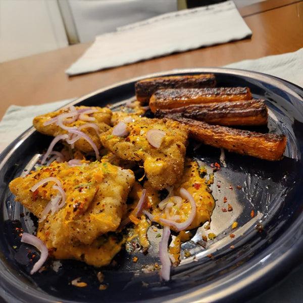 Spiced fish fillets with roasted carrots and red onions on a black plate, fresh seafood meal