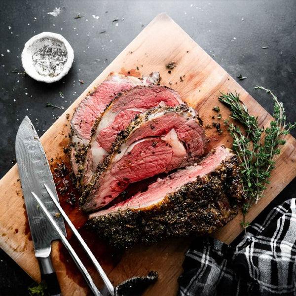 Sliced prime rib roast with herbs on wooden board, ready to serve