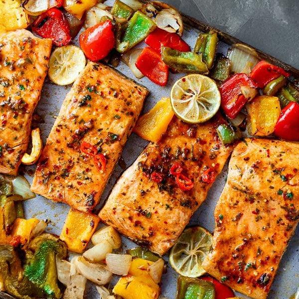 Roasted salmon fillets with bell peppers, onions, and lemon slices for a fresh seafood meal.