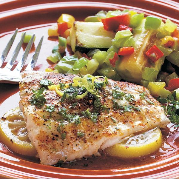 Grilled fish fillet with lemon slices and herbs, served with zucchini and bell peppers on a red plate