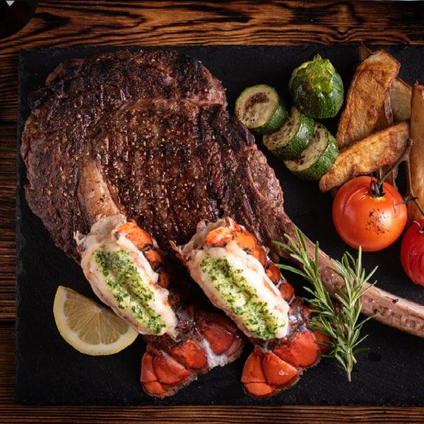 Grilled steak with lobster tails, zucchini, tomatoes, and rosemary on slate — fresh seafood & steak meal