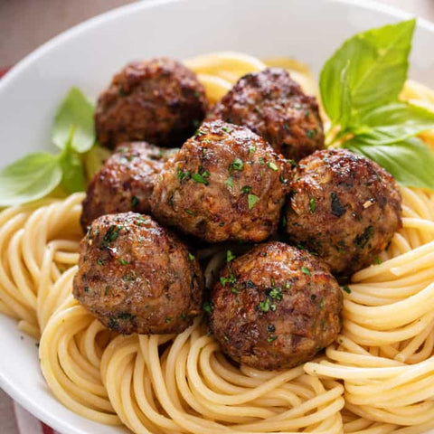 Spaghetti with meatballs and fresh basil, served in a white bowl with marinara sauce nearby